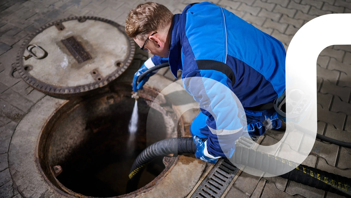 Ein Mitarbeiter von REMONDIS kniet am geöffneten Fettabscheider und führt eine Hochdruckspülung durch