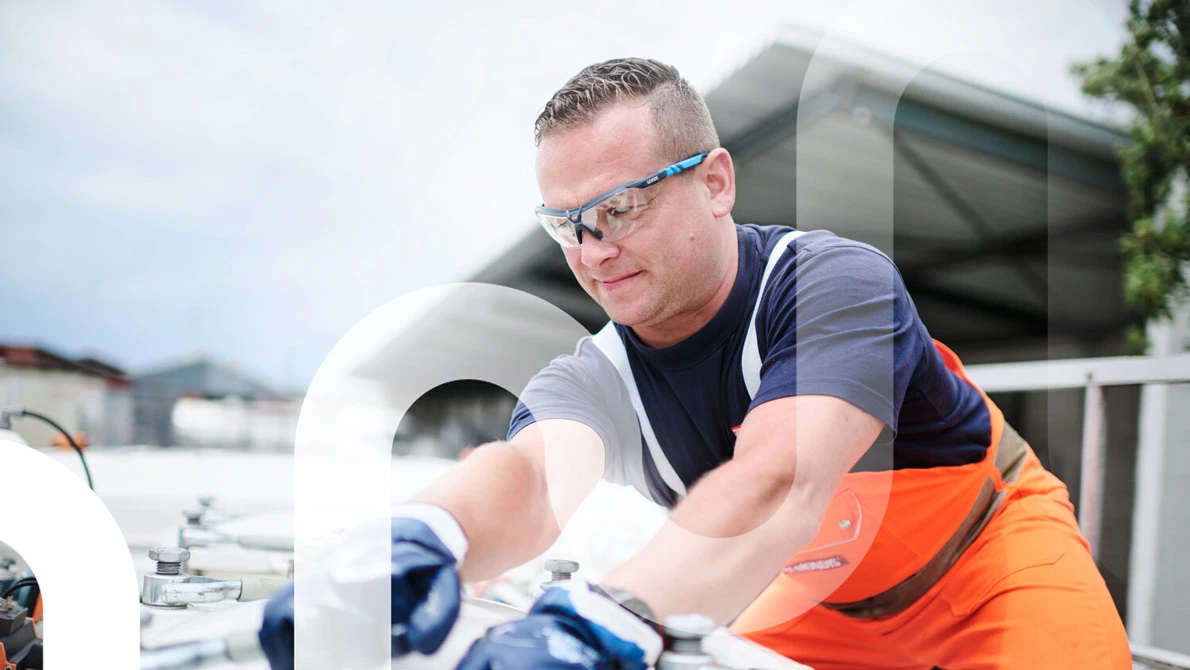 Ein Mitarbeiter von REMONDIS kniet am geöffneten Fettabscheider und führt den Saugschlauch hinein. Im Hintergrund leuchten die Fenster der Restaurantküche.