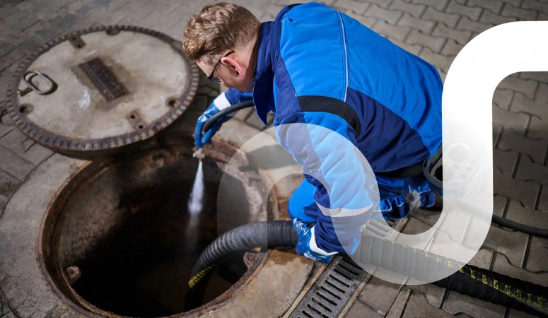 Ein Mitarbeiter von REMONDIS kniet am geöffneten Fettabscheider und führt eine Hochdruckspülung durch.
