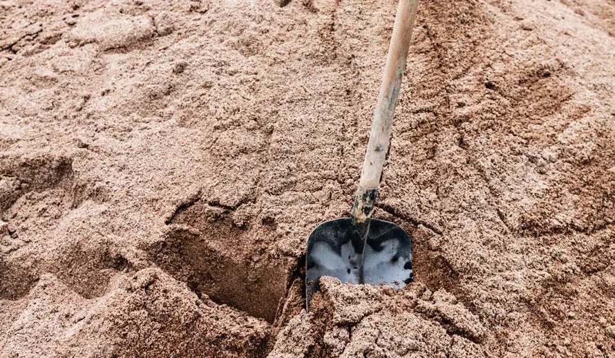 In einem Sandhaufen einer Baustelle steckt eine Schaufel.