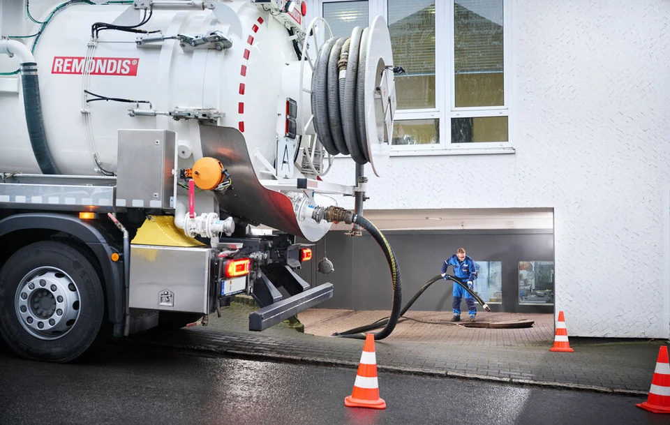 Remondis Saug-Druck-Tankfahrzeug vor einem Hotel, im Hintergrund führt ein Mitarbeiter den Saugschlauch in den Abscheider