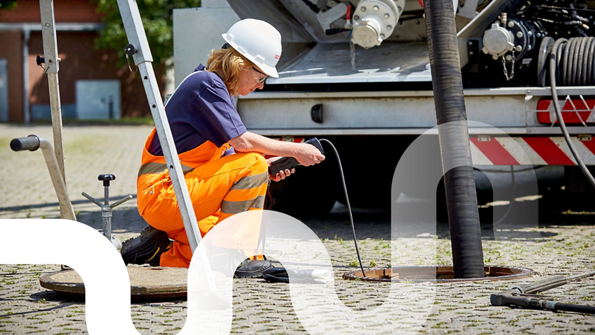 Eine Mitarbeiterin mit Schutzhelm schaut auf das Display ihres Messgerätes, dessen Messfühler in den Abscheider führt. Im Hindergrund steht ein Saug-Druck- Tankfahrzeug.