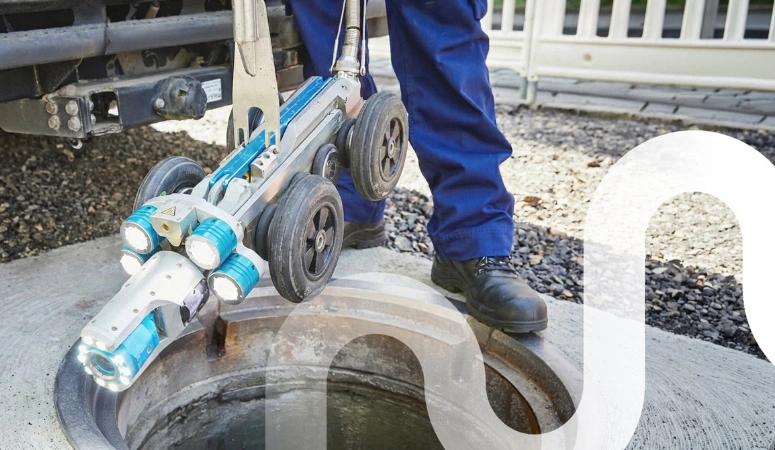 Eine Inspektionskamera auf vier Rädern wird zur Kanaluntersuchung in einen Schacht hinabgelassen.