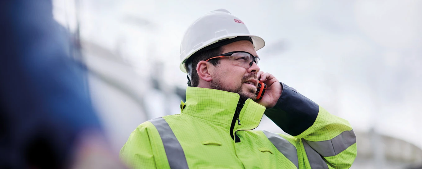 Mitarbeiter in Schutzkleidung steht im Freien und telefoniert.