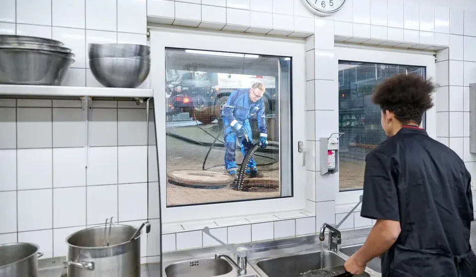 Koch blickt aus der Restaurantküche in Richtung Abscheider, wo ein Sauschlauch in den Abscheider geführt wird