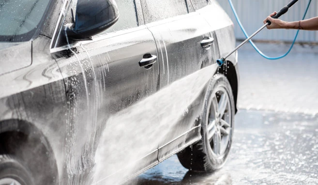 Ein PKW wird auf einem Waschplatz mit einem Hochdruckgerät gereinigt. Die ölhaltigen Abwässer fließen über den Boden.